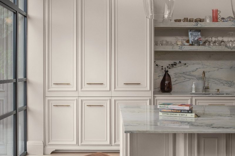 A contemporary kitchen with decorative cabinetry doors, marble surfaces and open shelves, and wood bar stools.