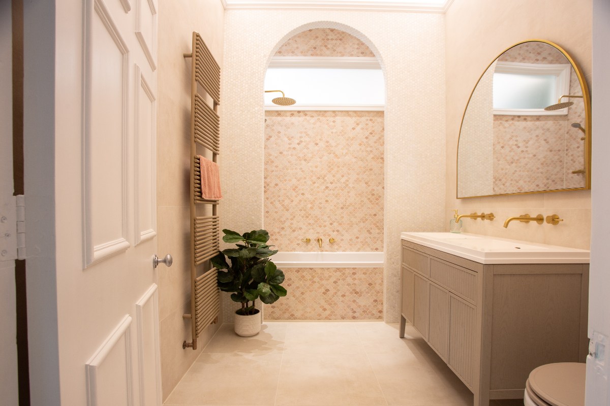 A calm bathroom design with a shower-bath nook, a double vanity unit with an arched mirror, a brass towel rail and house plants.