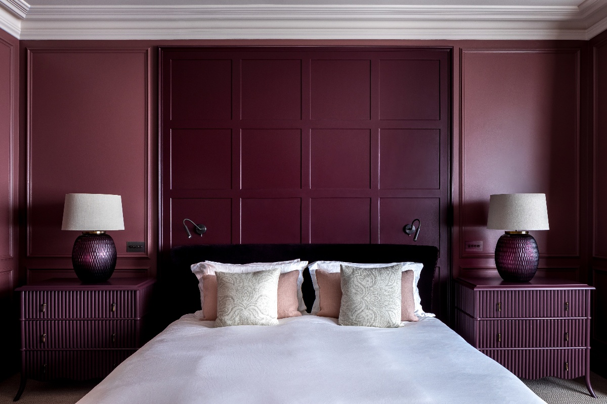 A purple drenched bedroom with matching fluted burgundy side tables, matching table lamps and a central bed.