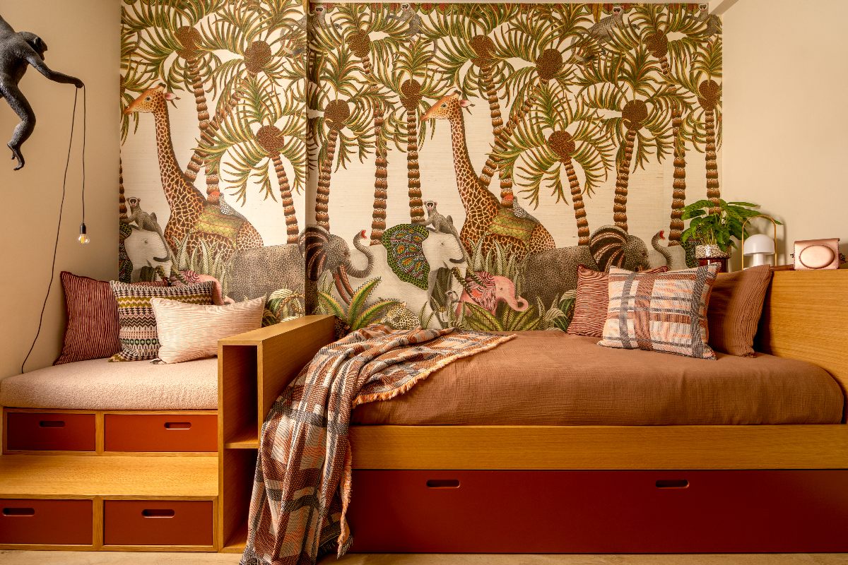 A kids bedroom with safari-inspired walls, wood and red bed and reading nook and patterned cushions.