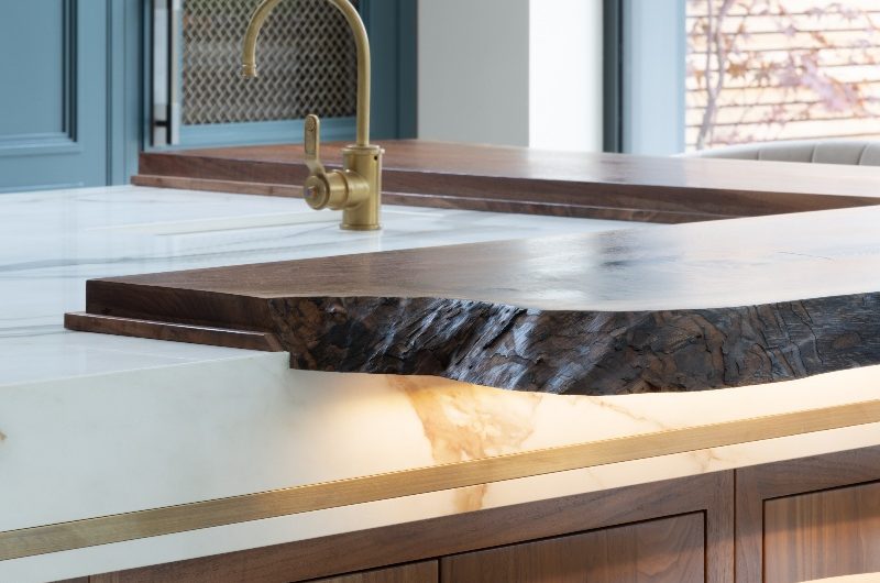 Closeup at an island with a wood breakfast bar with LED lighting underneath, porcelain worktops, and a compact sink and tap.