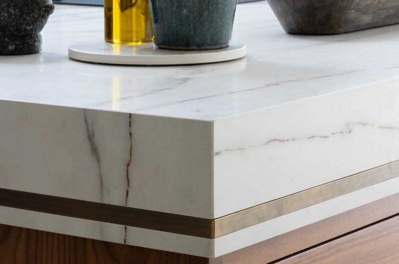 Closeup at the materials used in the contemporary kitchen, such as wood, veiny porcelain, and brass trims.
