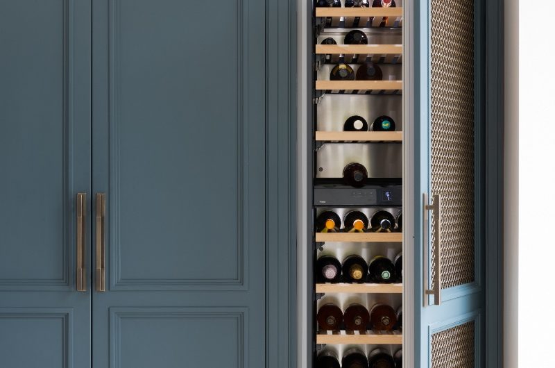 A long wine fridge concealed behind a mesh and dark blue decorative door panel.