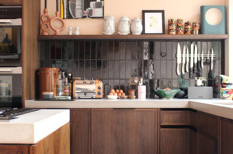 A mixed style kitchen with wood cabinets, terrazzo flooring, dark tile splashback, and pale pink wall paint.