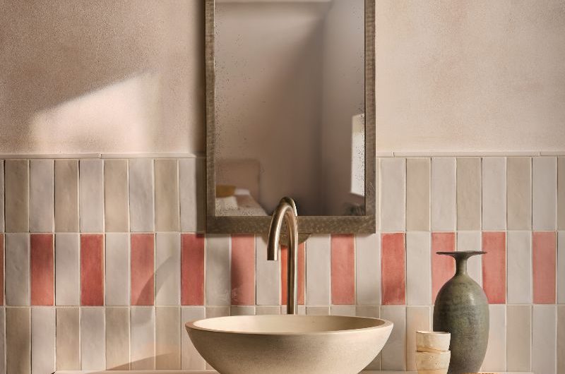 A vanity area with stacked metro tiles in neutral and light pink colours, with a wall-mounted countertop with a basin on top, and minimalist decor.