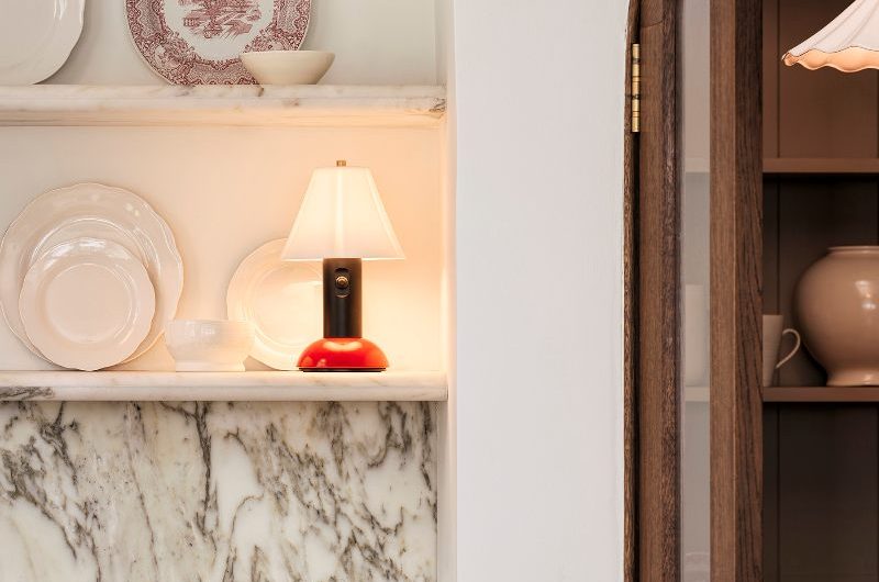 A modern kitchen with dark units, marble surfaces, floating shelves decorated with plates, and a wood pantry.