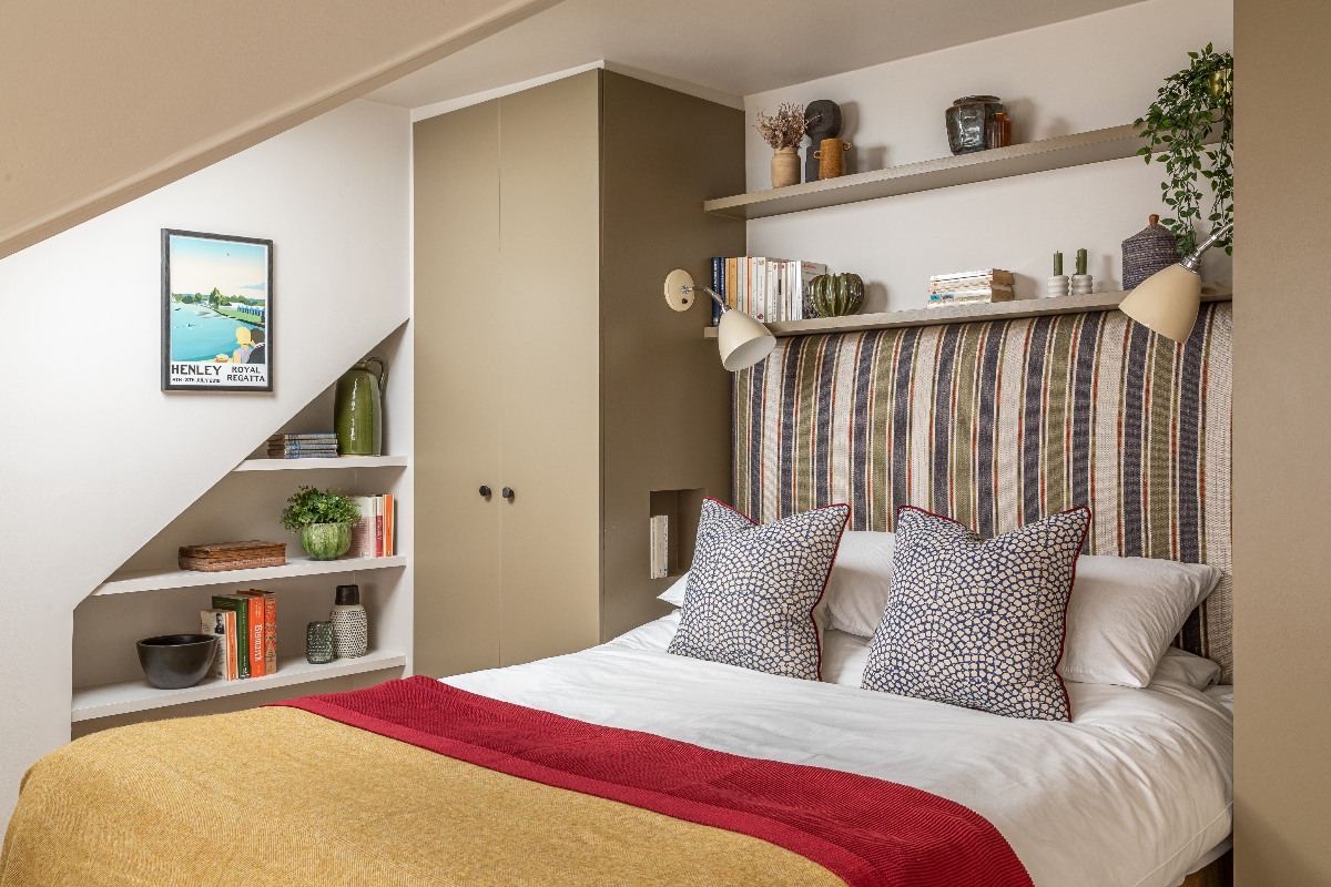 A bed frame tucked beneath the angled ceiling, with a striped headboard and colourful soft furnishings.