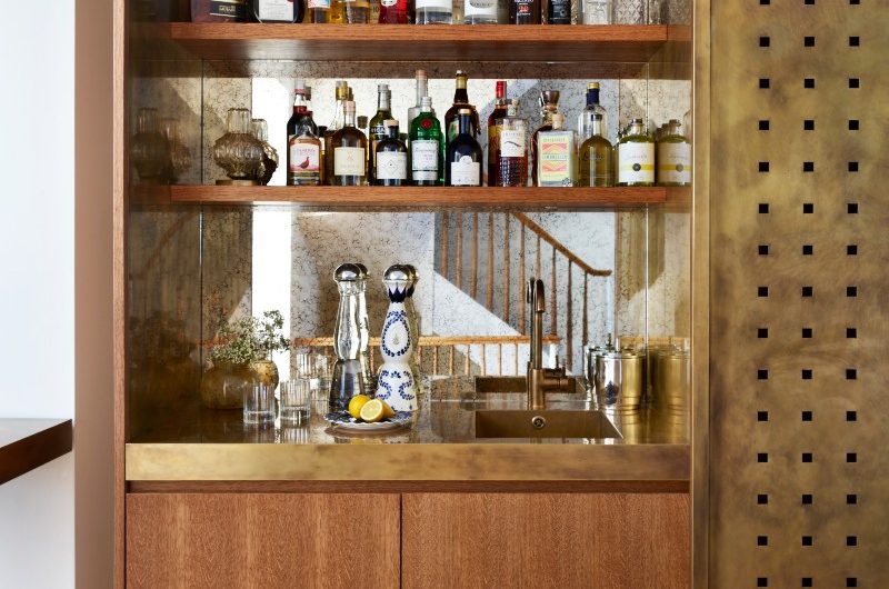 A home bar design with wood base cabinet, aged mirror splashback, metallic worktop and sink, and wood open shelves.