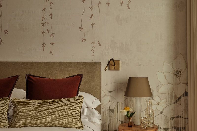 A calm and quiet bedroom design with floral wallpaper, plush carpet, an olive bed frame and wood side table.