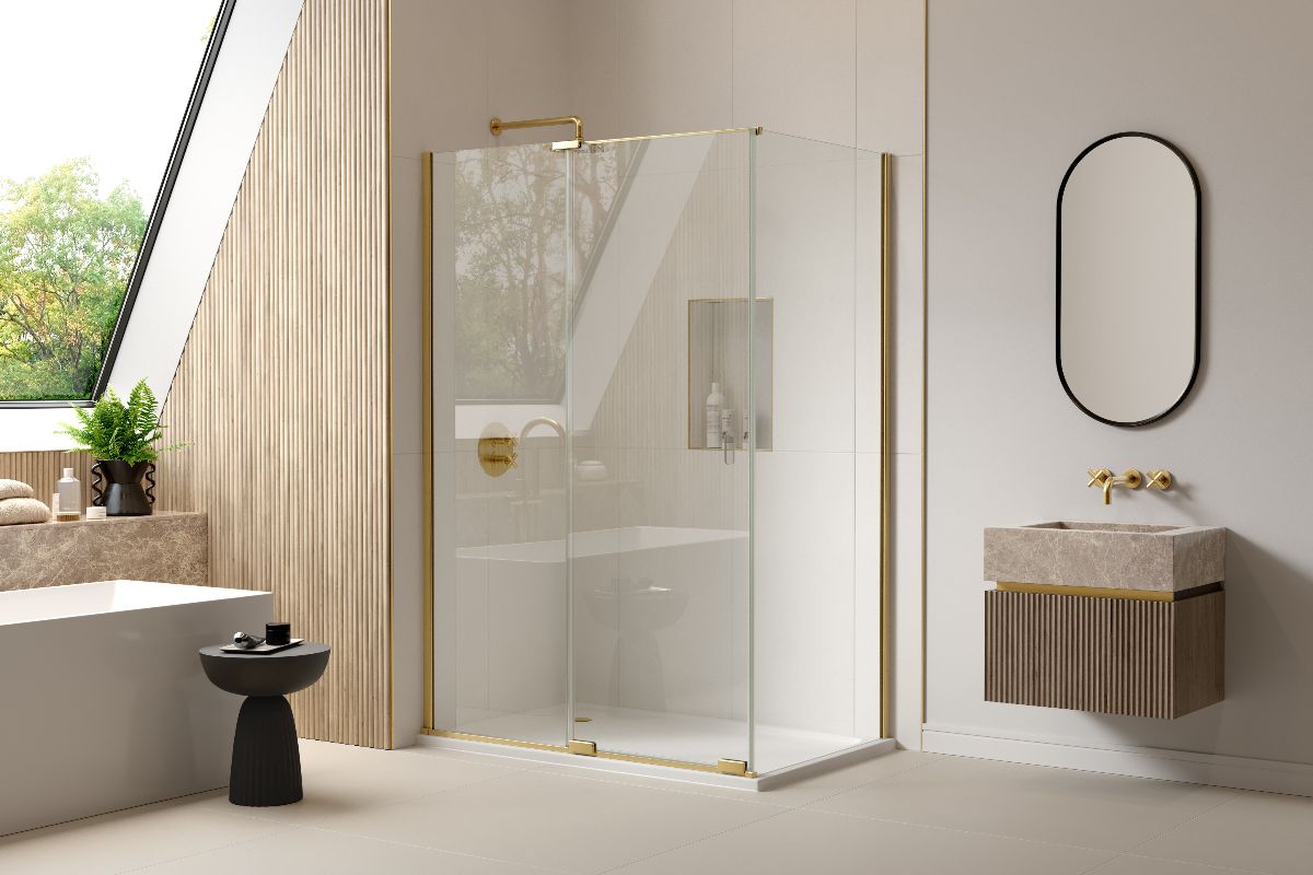 A modern bathroom design with a shower zone with glass and brass enclosure, a freestanding tub near the window, and a wall-mounted basin and vanity on the opposite side.