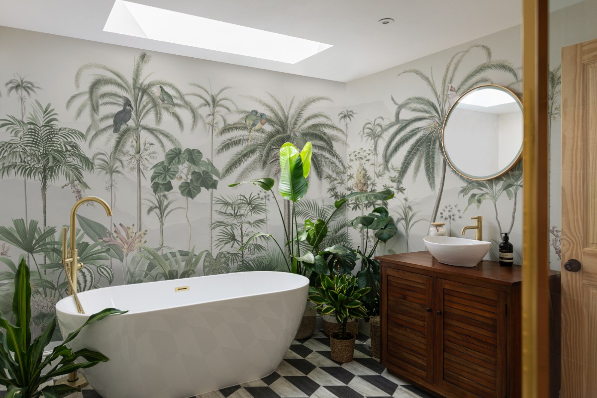 A bathroom camping scheme with a wood vanity with a countertop basin, exotic wall murals, and a freestanding bath surrounded by house plants.