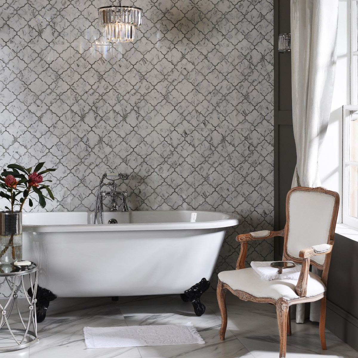 An elegant scheme with marble wall and floor tiles, a freestanding tub, and a classic chair.