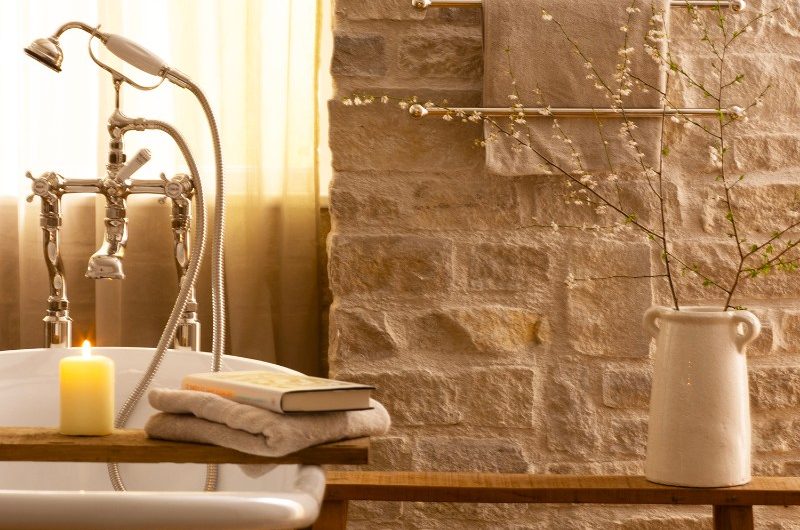 A neutral scheme with exposed brick walls, towel rails, and a metallic bath, a wooden bench.