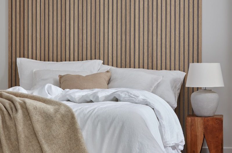 A neutral bedroom design with wood flooring, comfortable rug, wood panelling, and white bed linen.