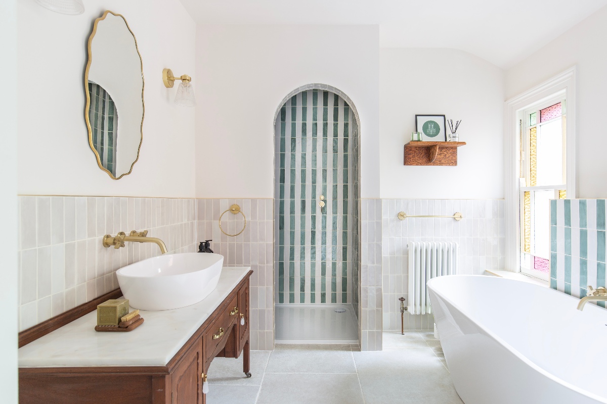 A big bathroom design with a large wood vanity, a freestanding bath and a shower zone with a curved entryway and striped tiles.
