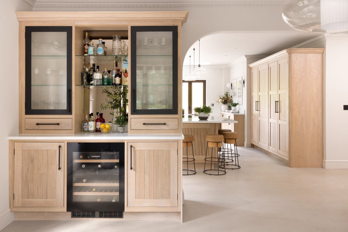 A home bar with two black-framed fluted glass doors, antique mirrored glass, open shelving, and quartz worktops near the main kitchen.