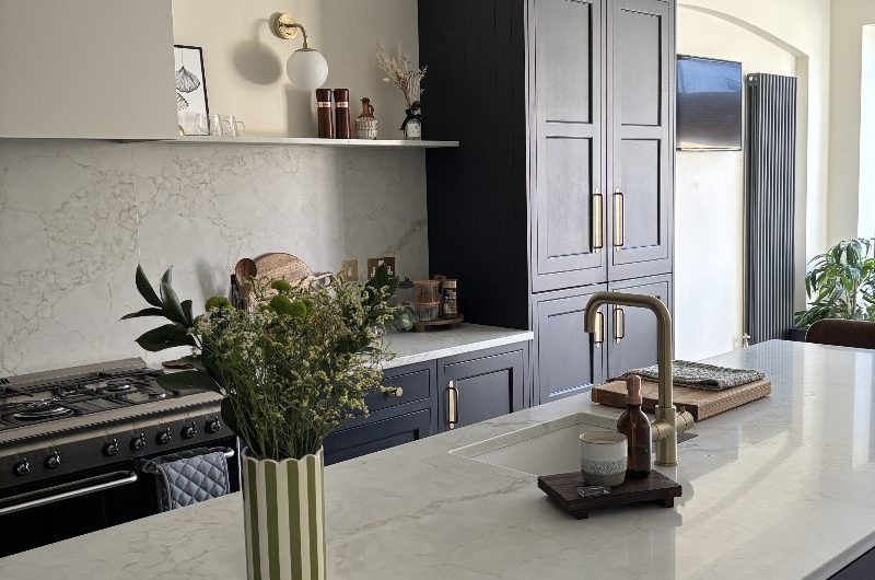 A dark kitchen design with light work surfaces and brass details.