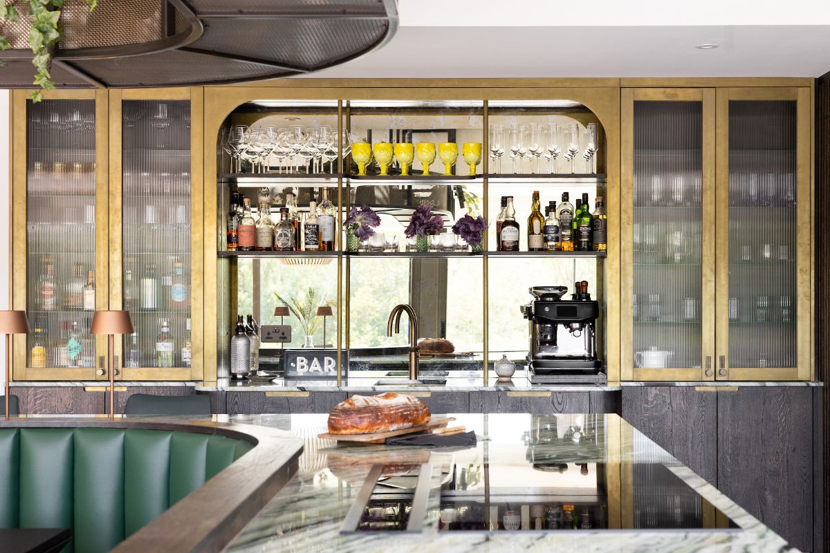 An Art Deco kitchen design with wood furniture, brass upper cabinets, mirrored splashback, a drinks zone, and central island.