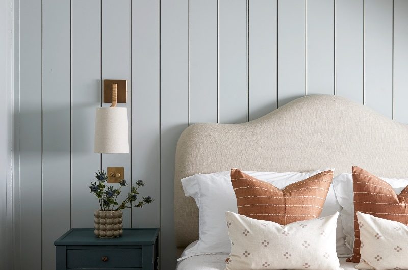A serene sleep space with wall panelling, a neutral headboard, minimalist bobbin bedside table and brass lighting.