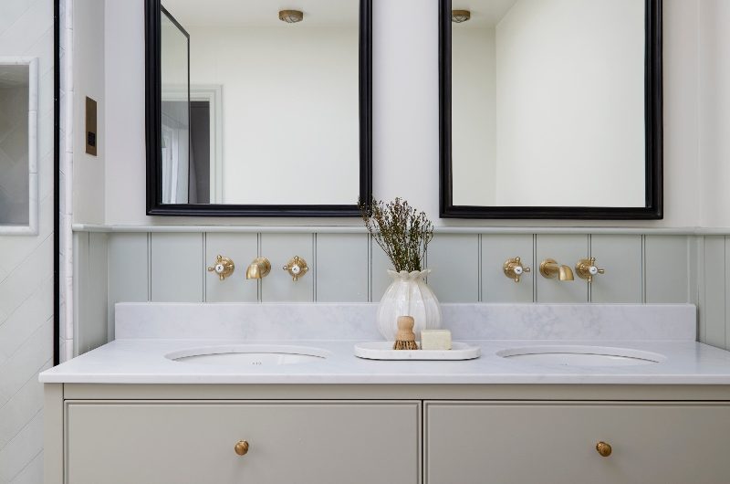 A wetroom with a double vanity, matching black framed mirrors above it and wall lighting, and sage green panelling behind the unit.