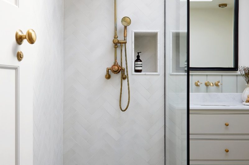 A walk-in shower in a neutral wetroom with herringbone and hexagon tiles and a classic, brass shower system.