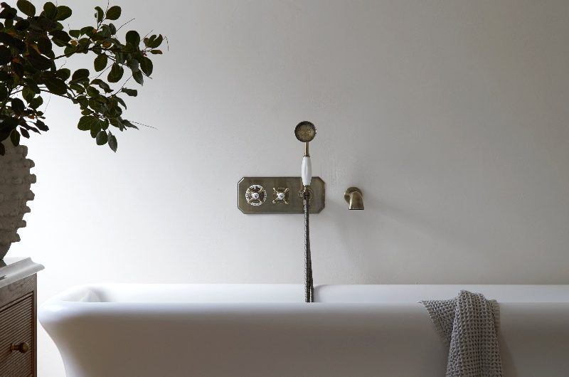 Closeup at a classic, neutral bathroom with a freestanding tub, classic bath filler, and a wood vanity.