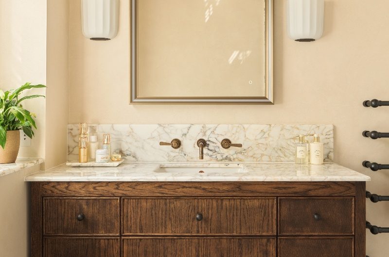 A wood vanity topped with veiny surfaces, with an inset sink, classic square mirror and wall lights.