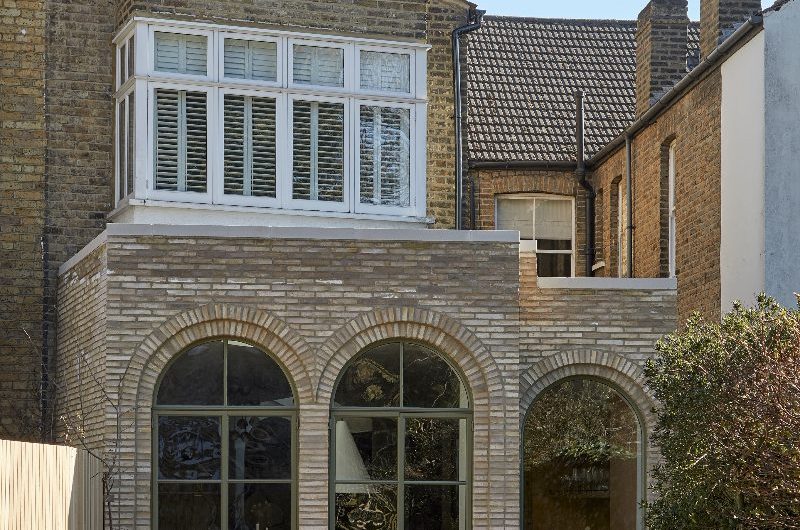 A period property with three brick arches with metal-framed glazing finished in an earthy green tone.