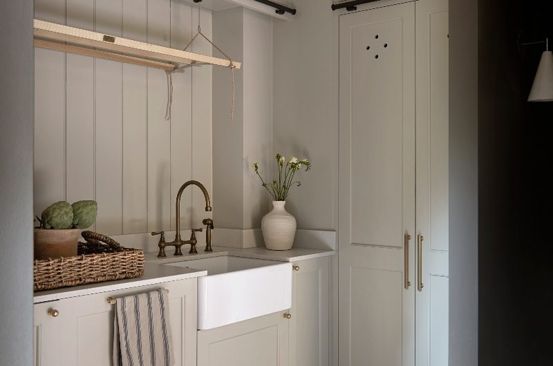 A utility room with neutral cabinetry, a butler sink and brass tap, and a hanging drying rack.