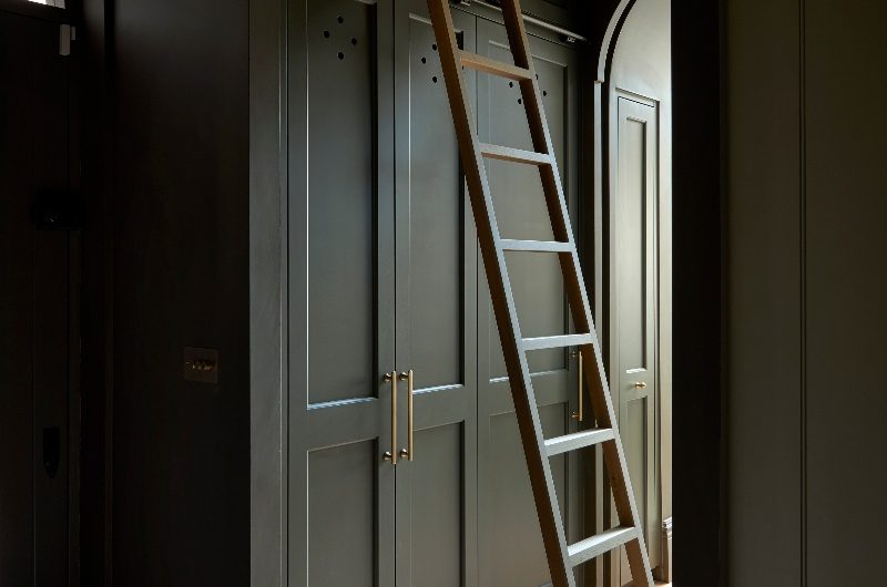A utility room with tall dark green units, a ladder, and terracotta flooring.