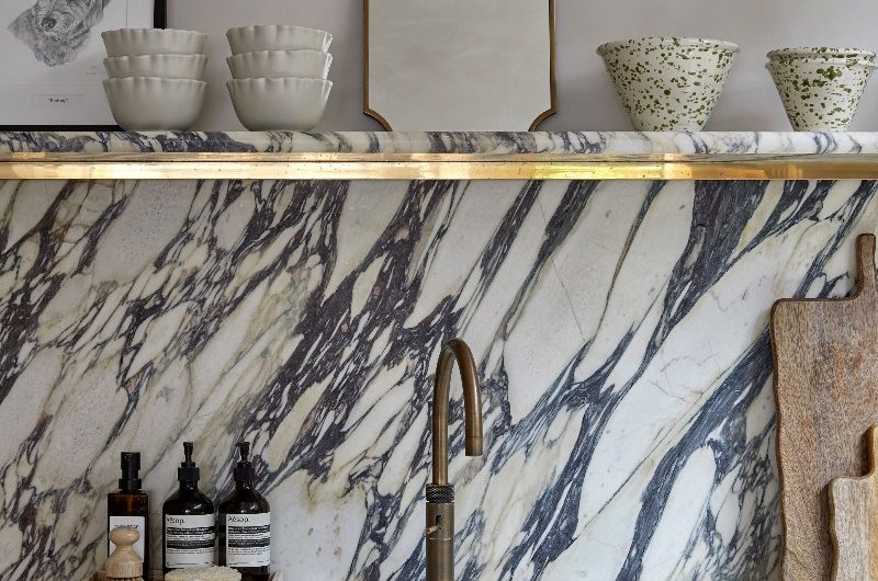 A sink zone with statement Calacatta Viola marble, a brass tap, and matching stone shelf, and base wood cabinets.