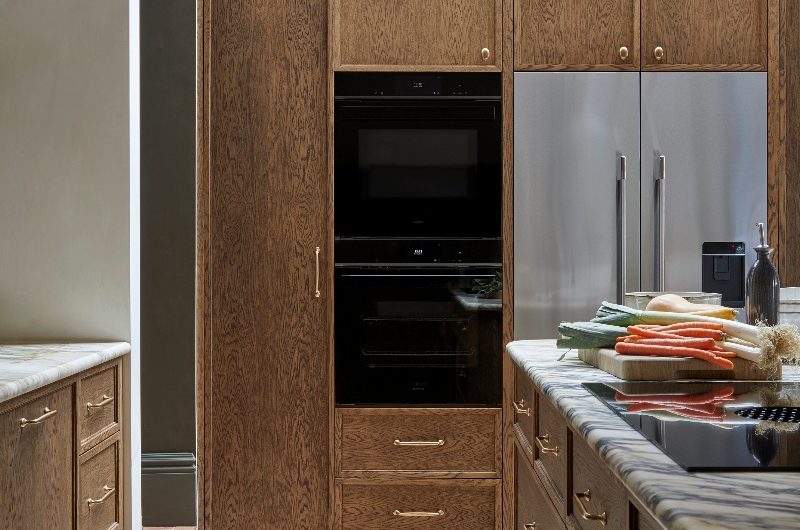 Tall wood cabinets with built-in ovens and double door fridge-freezer with skylights above it.