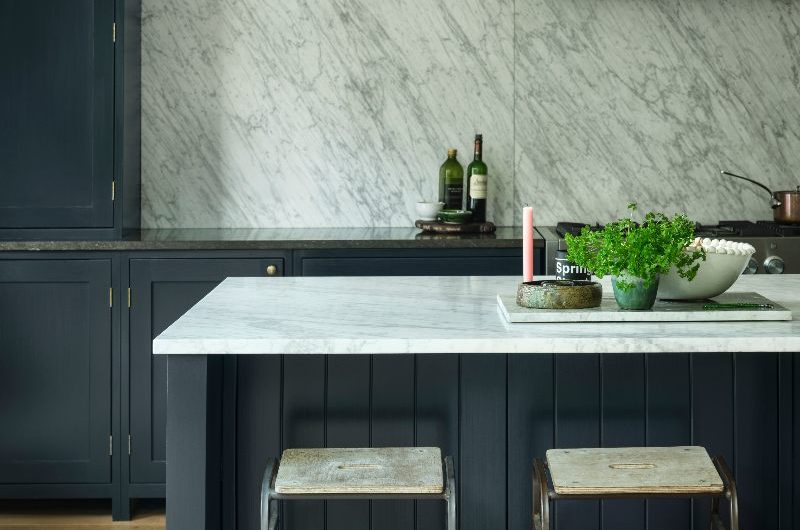 A timeless kitchen design with dark blue cabinetry and island, with veiny work surfaces, and wood flooring.