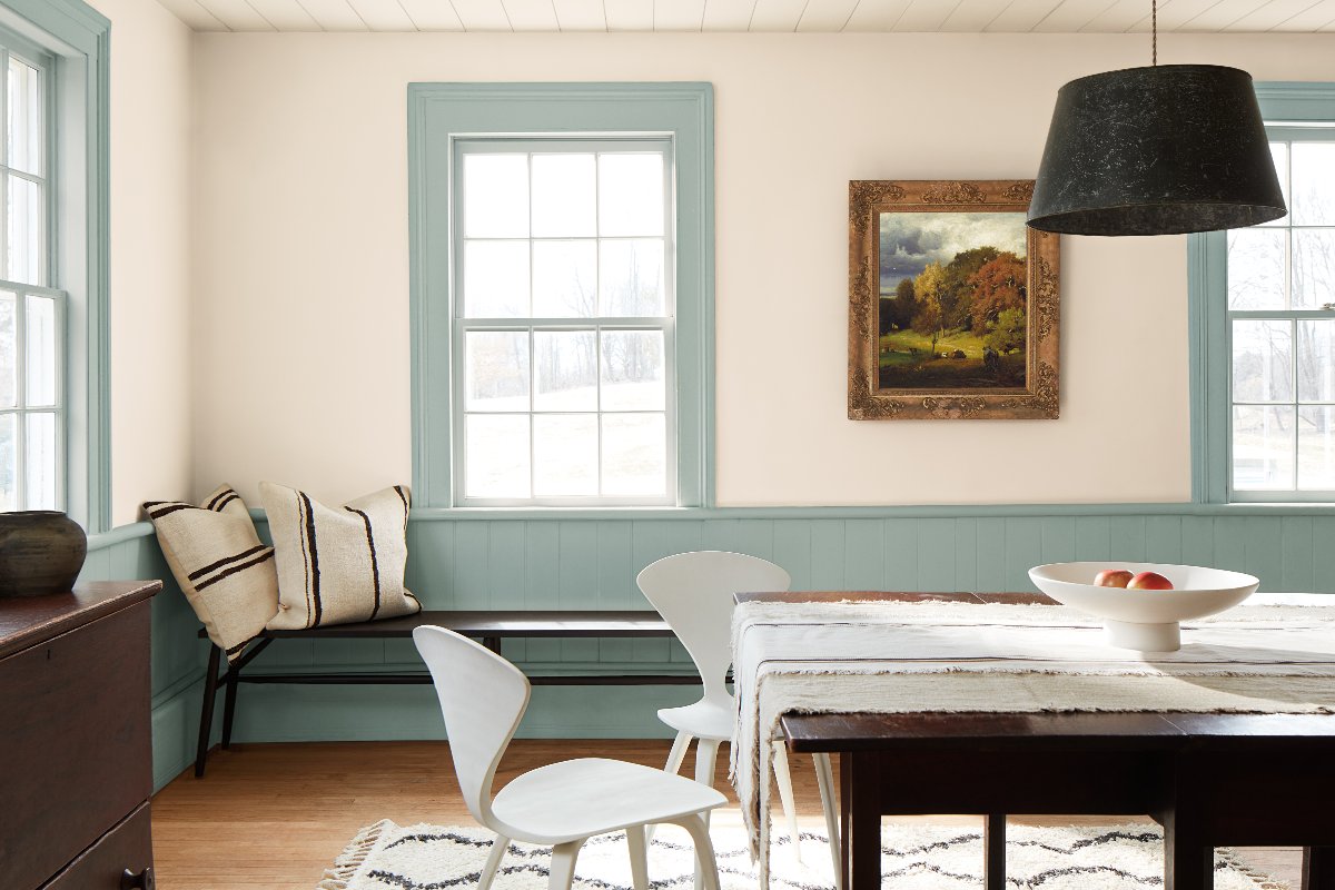 A dining room with neutral wall paint and a blue shade on the woodwork, with a bench and wood dining table.