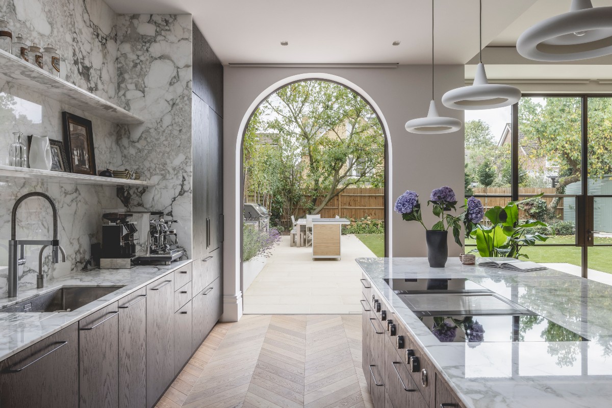 A kitchen extension with herringbone flooring, arched windows, marble surfaces, and minimalist lighting.