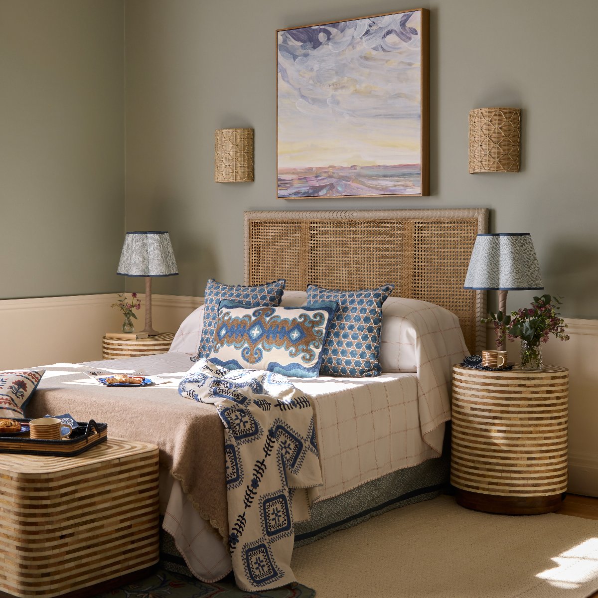 A chic bedroom design with a cafe feeling, a rattan bed, striped bedside table, patterned bed linen, and blue table lamps.