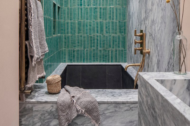 A bath area with marble surround, green wall tiles, and gold brassware.