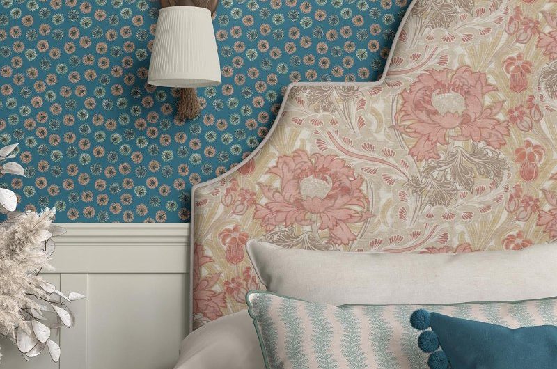 A blue bedroom design with white panelling, floral wallpaper, a floral headboard, and colourful cushions.