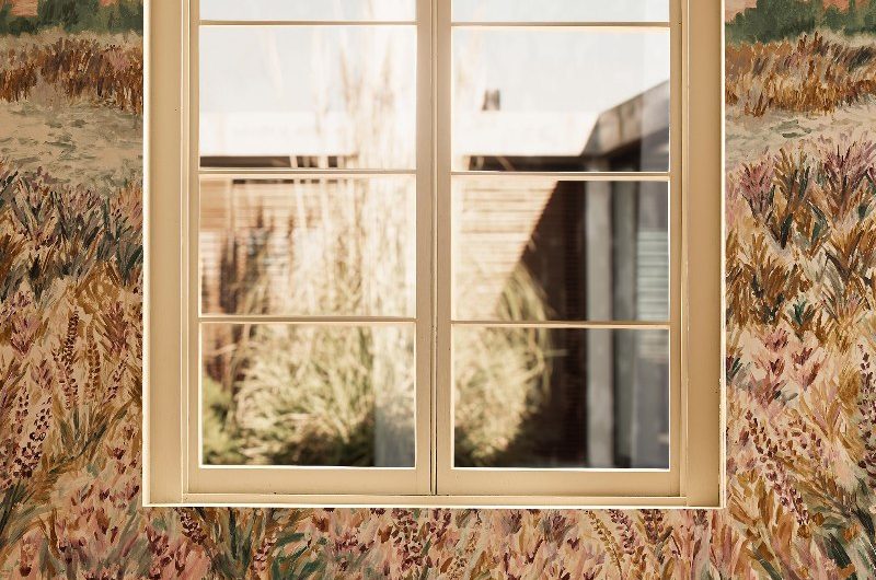 A living room with floral wallpaper and a velvet armchair in a burnt orange shade.