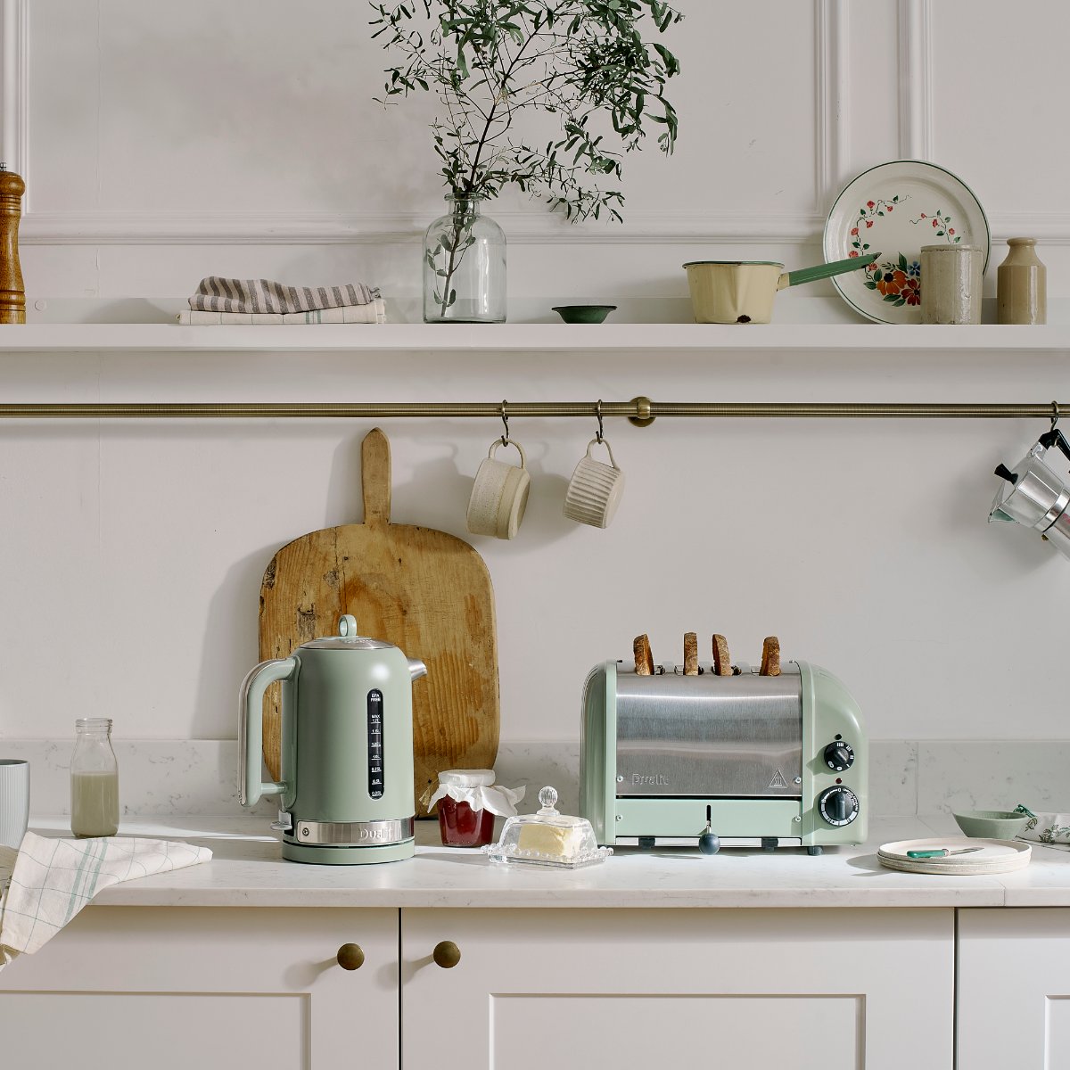 A classic Shaker kitchen with elegant countertops, open shelving, a brass rail, and a sage green kettle and matching toaster.