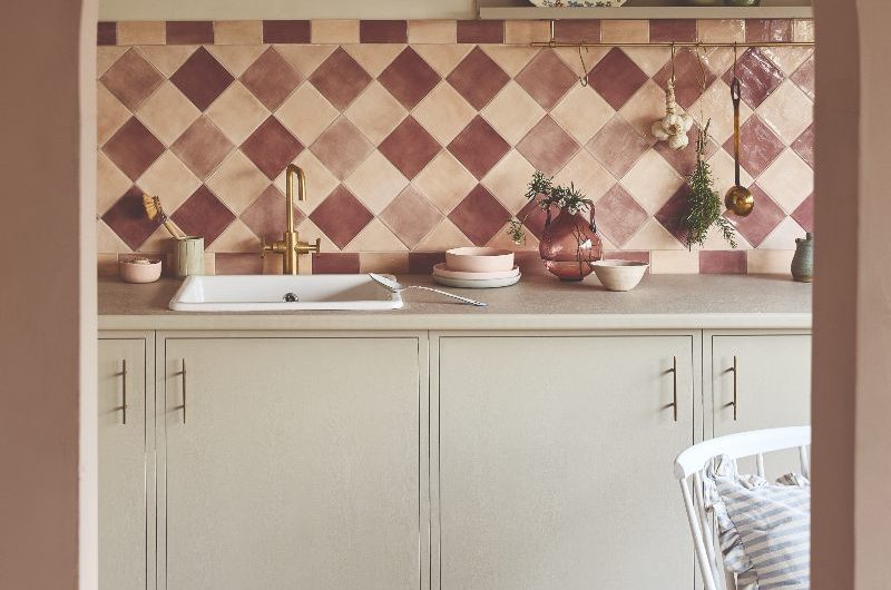Classic kitchen with a splashback clad in diamond-shaped tiles in a checkered pattern in peach and pale burgundy shades, with neutral cabinets and work surfaces.