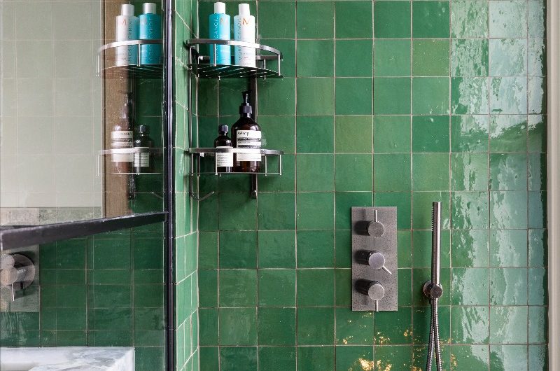 A shower area with green zellige tiles, brushed chrome fittings and a corner-mounted storage caddy.
