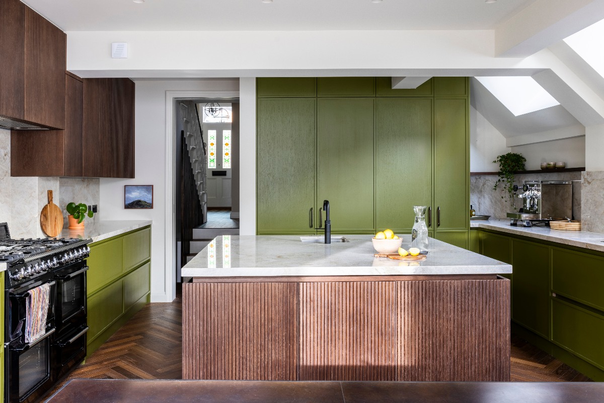 A kitchen design with a U-shaped layout, a central island and adjoining dining area, flooded with light through glazing.