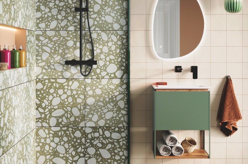 A modern bathroom design with a terrazzo-drenched shower with matt black shower system, and an adjoining vanity area with a green wall-mounted unit and a smart mirror.