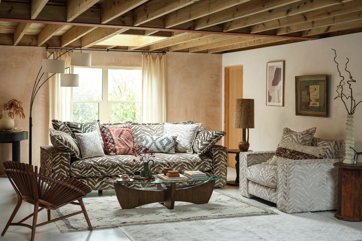A rustic living room with zebra printed sofa and armchair, with wooden beams, and paster walls.