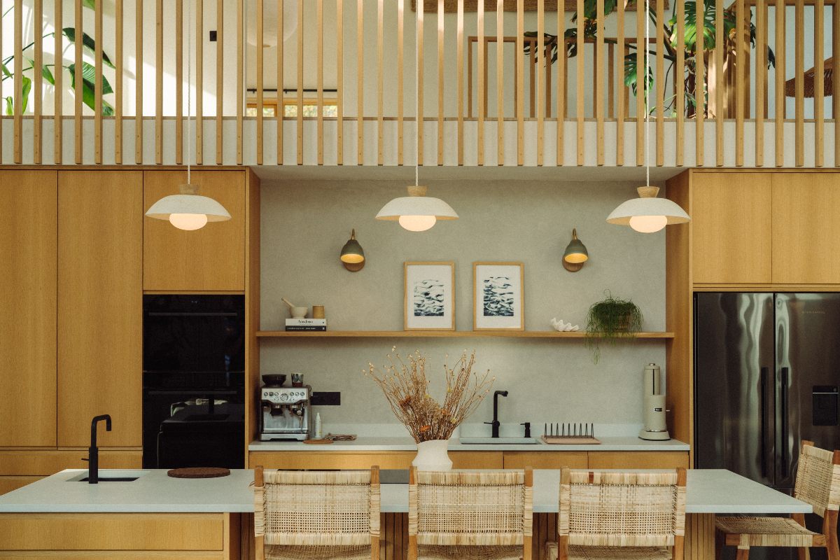 Wood kitchen with minimalist decor, layered lighting, a central island with seating, rattan bar stools, pared-back work surfaces and natural materials.