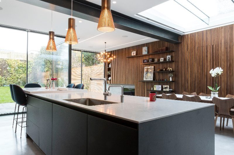 A modern kitchen design with handleless cabinetry, a central island and tall fluted wood wall panelling.