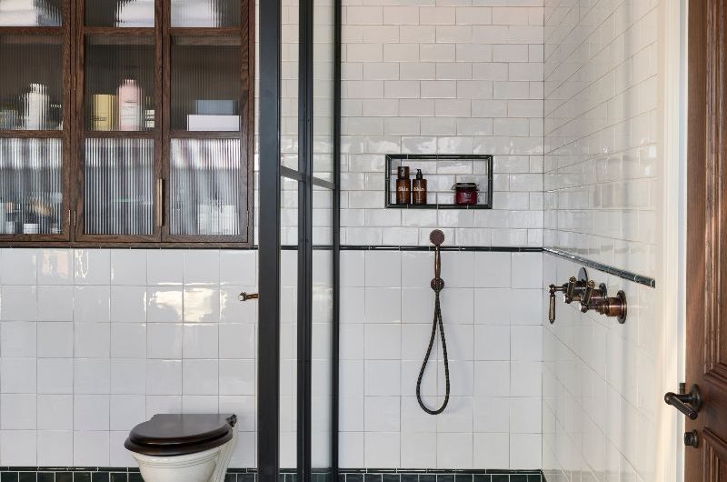 A timeless wetroom with shower niches, a steel-framed partition with a toilet next to it and a wall-mounted wood cabinet.