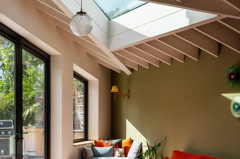 A snug with terracotta floor tiles, green wall paint, an orange sofa, and smart storage.