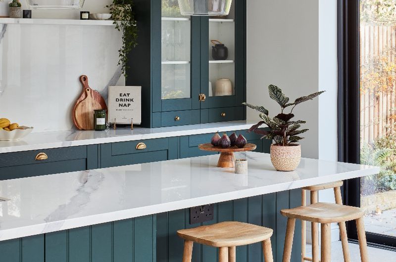A Shaker kitchen with repainted units, a panelled island, glazed cupboard and minimalist wood decor.